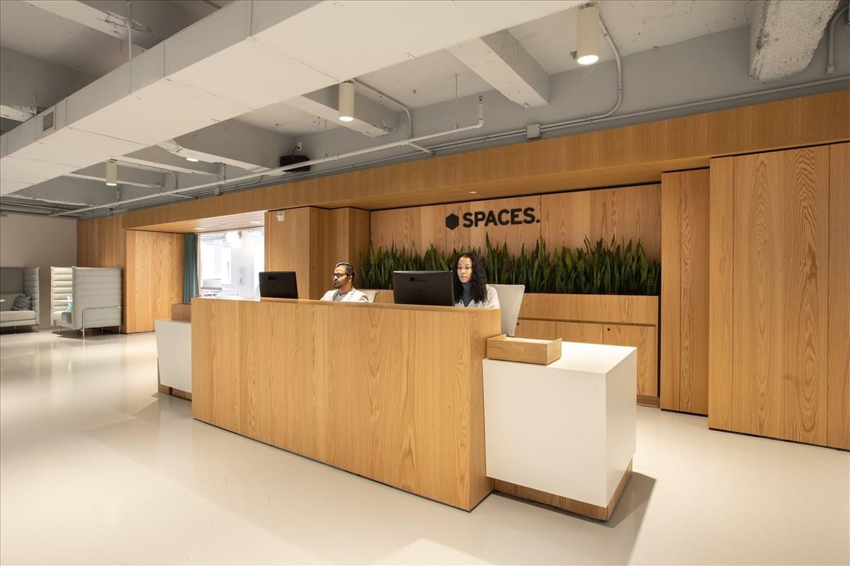 Wooden reception desk with the Spaces logo and lush greenery in the background.