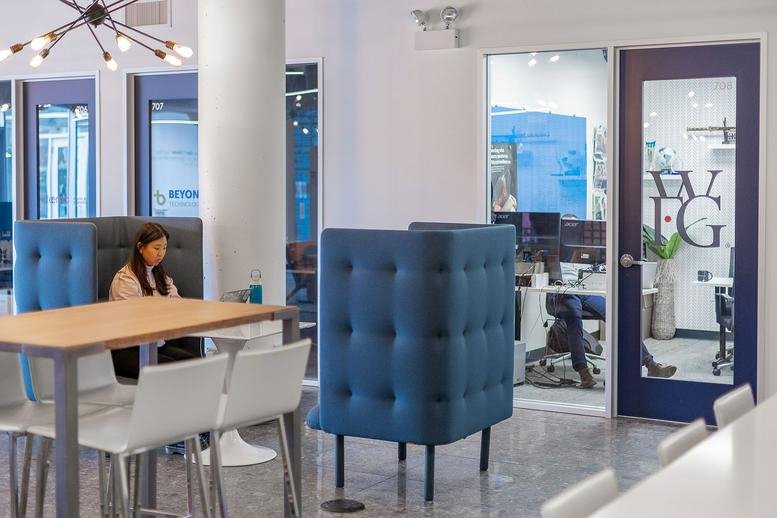 Modern coworking lounge at 405 W Superior St featuring blue privacy pods and a communal wooden table.