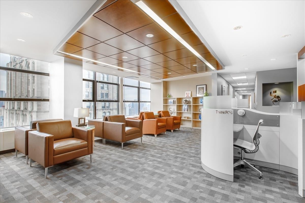 Bright lounge area with leather armchairs, wooden ceiling panels, and a reception pod.