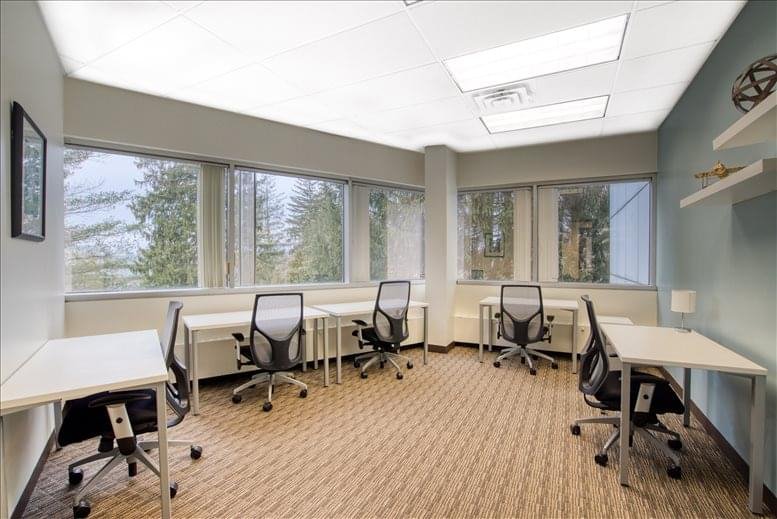 Spacious shared workspace with multiple desks, ergonomic chairs, and large windows with natural light.
