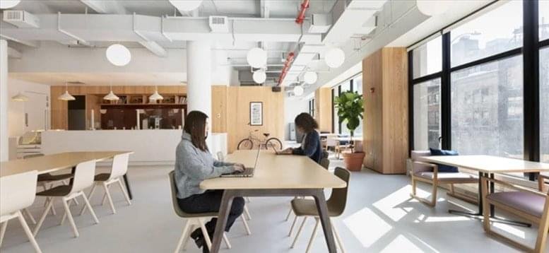 Spacious communal lounge at 413 West 14th Street, New York City with wooden tables and large windows.