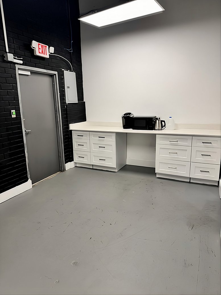 Work area with white cabinets and an exit door set against a black brick wall.