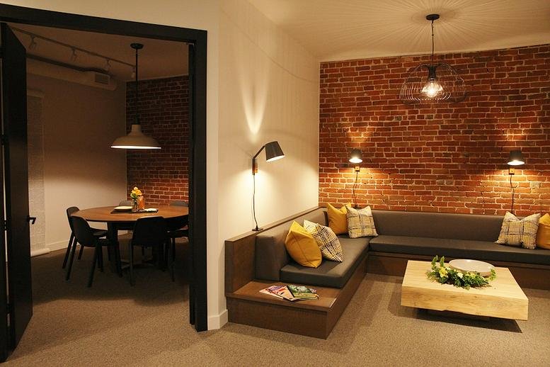 Spacious lounge and dining area with brick walls, warm lighting, and a view into a meeting room.