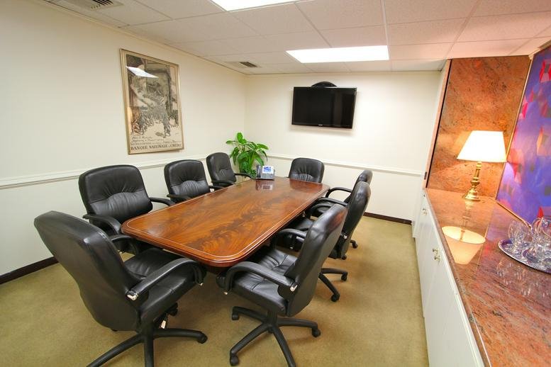 Professional boardroom featuring a large polished wood table and black leather chairs.