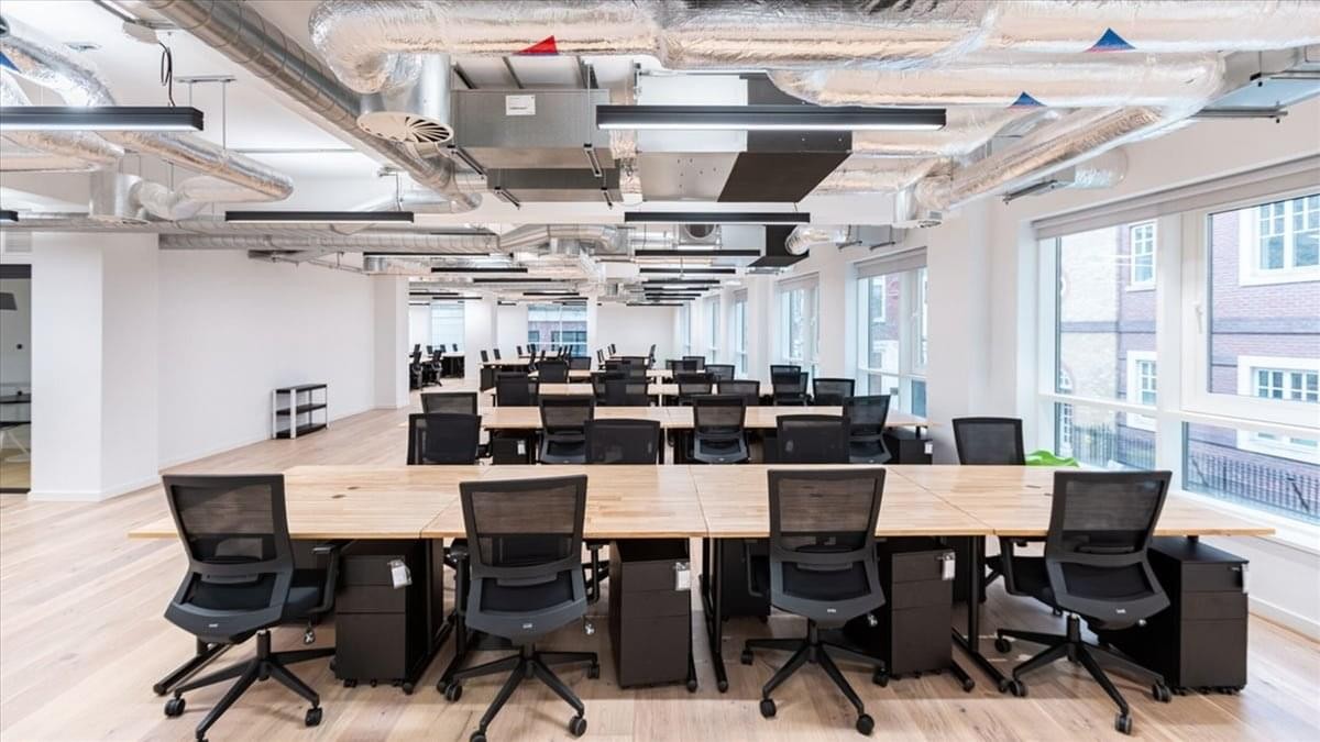 Open-plan office at 421 7th Ave, SW, Calgary with wooden desks, black ergonomic chairs, and industrial ceilings.
