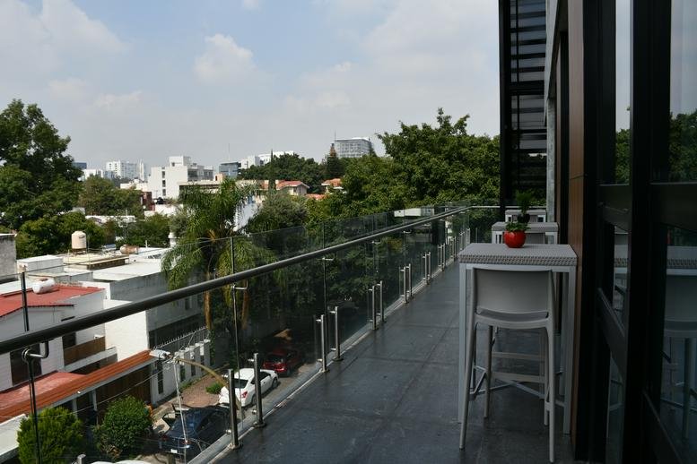Outdoor balcony terrace with a glass railing overlooking city trees and buildings.
