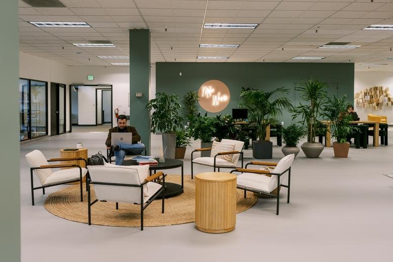 Spacious communal lounge at coLAB with modern armchairs, wooden tables, and lush indoor plants.