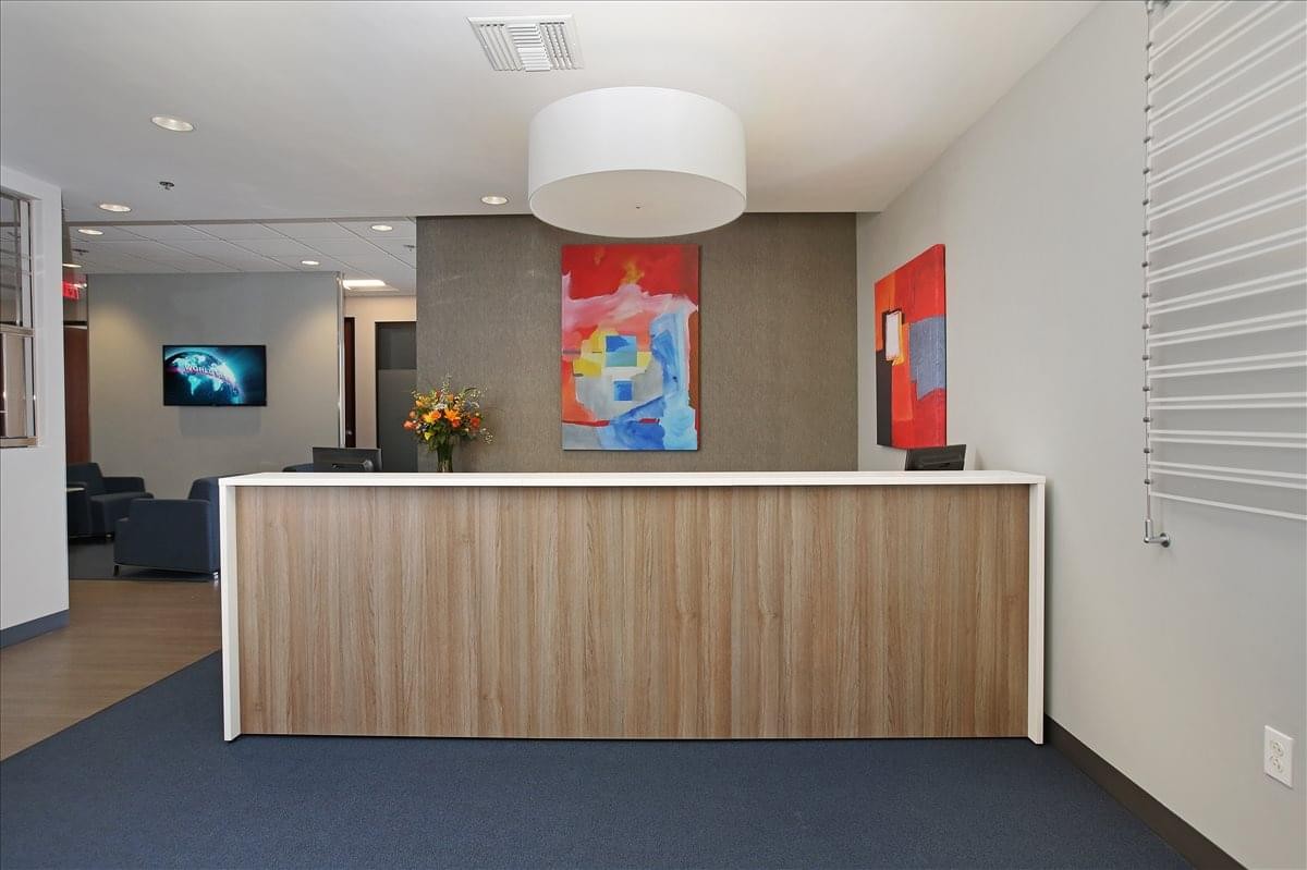 Reception area at 440 Stevens Avenue with a wooden front desk, drum pendant light, and colorful abstract art.
