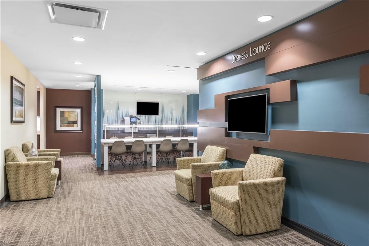 Modern lounge area at 445 Park Avenue, Suite 900/1000 featuring tan armchairs and a blue feature wall.