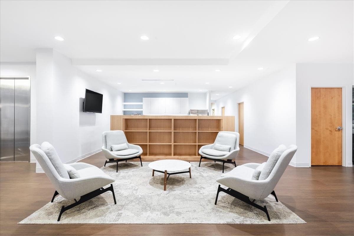 Contemporary lounge area at 4555 Mansell Road, Suite 300 with white armchairs and wooden shelving.