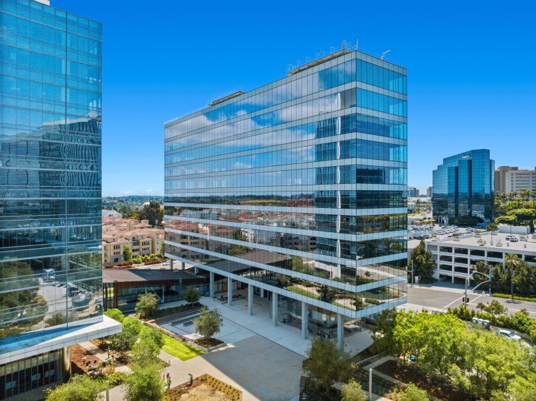 Exterior view of the glass-facade La Jolla Commons office building under a blue sky.