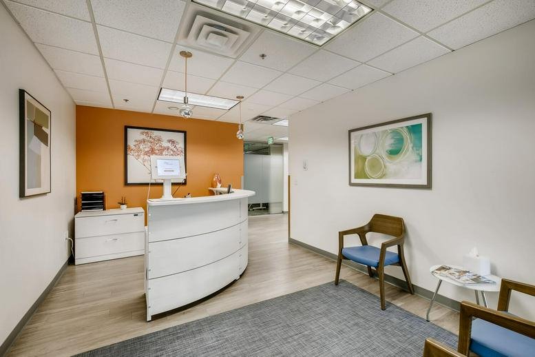 Bright reception area with an orange accent wall and white curved desk at 4845 Pearl East Circle, Ste 101.