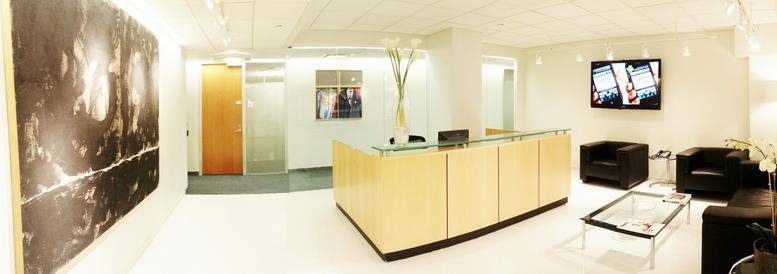 Bright reception area with a light wood front desk and black leather seating at 485 Madison Avenue.