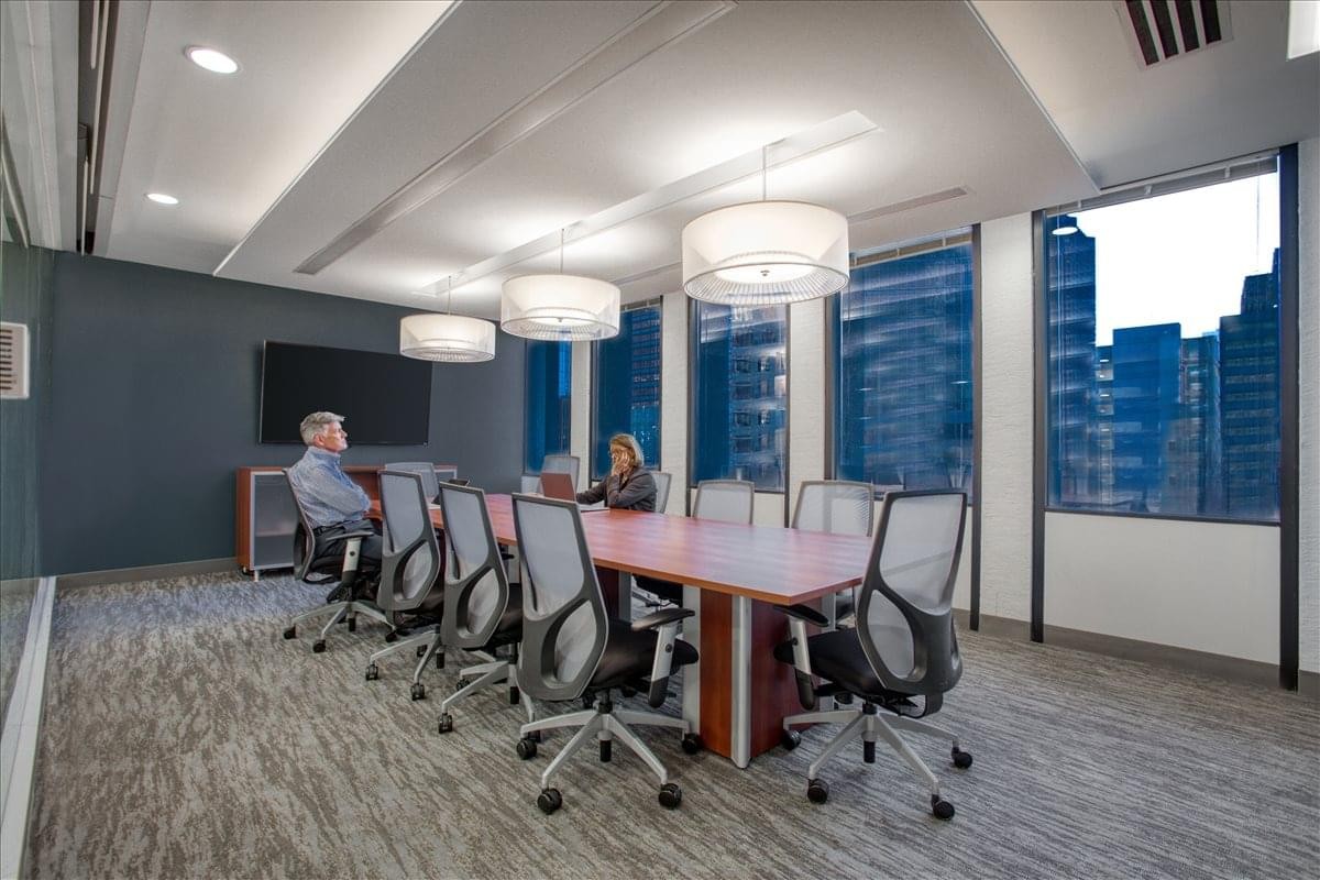 Executive boardroom with a large wood table, grey ergonomic chairs, and panoramic city views.