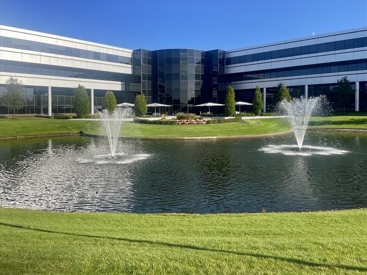 Well-maintained building exterior featuring two fountains in a large pond under a clear blue sky.