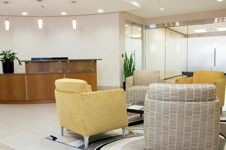 Spacious reception area at 50 West Broadway, 10th Floor, with a curved wooden desk and yellow armchairs.