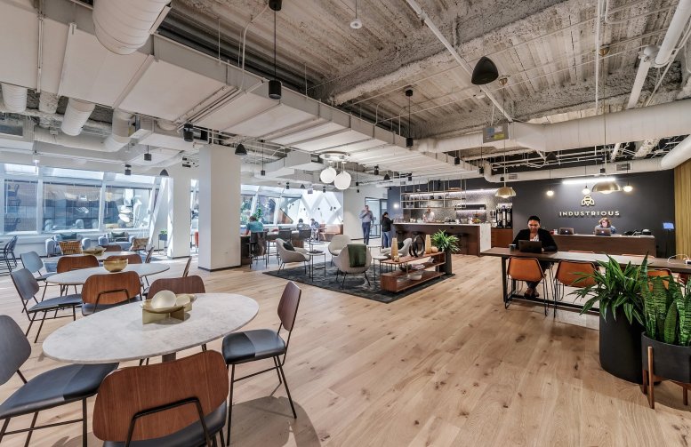 Spacious open coworking lounge with marble tables, mid-century chairs, and exposed ceilings.