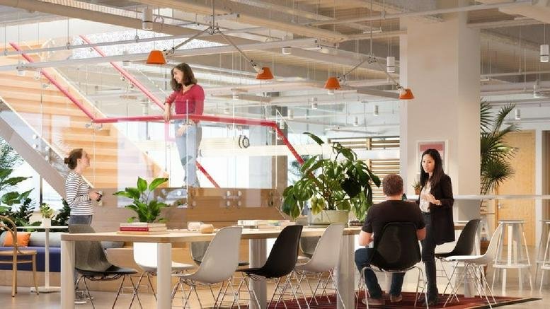 Spacious communal lounge at 501 East Kennedy Boulevard with people working at long wooden tables near a staircase.