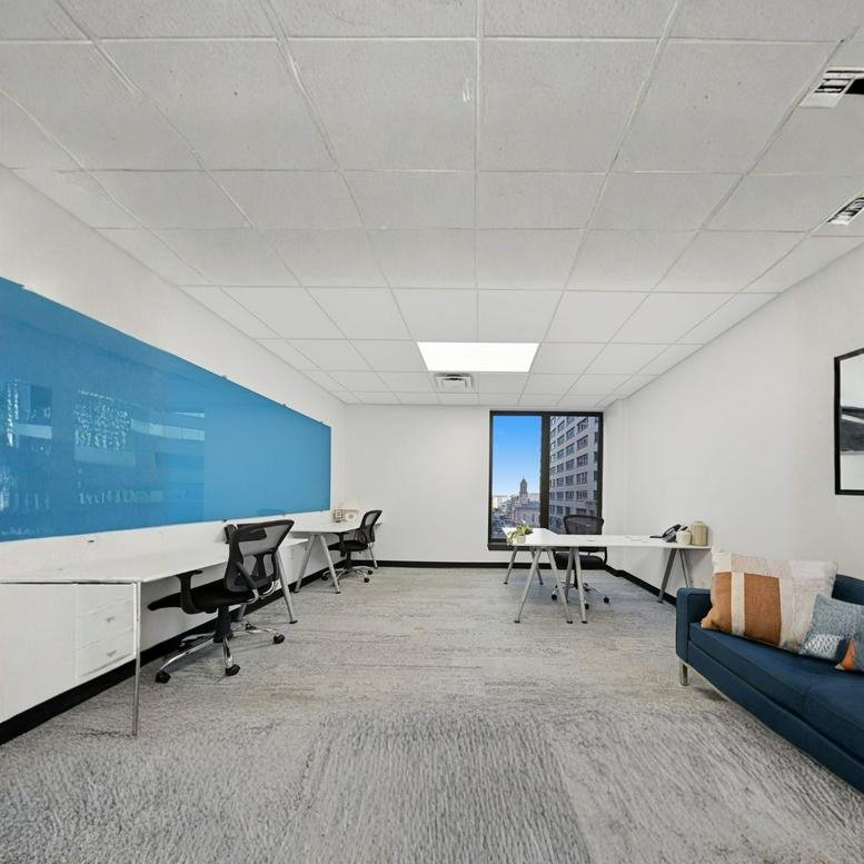 Spacious open-plan workspace with multiple white desks, blue accent wall, and a comfortable navy lounge sofa.