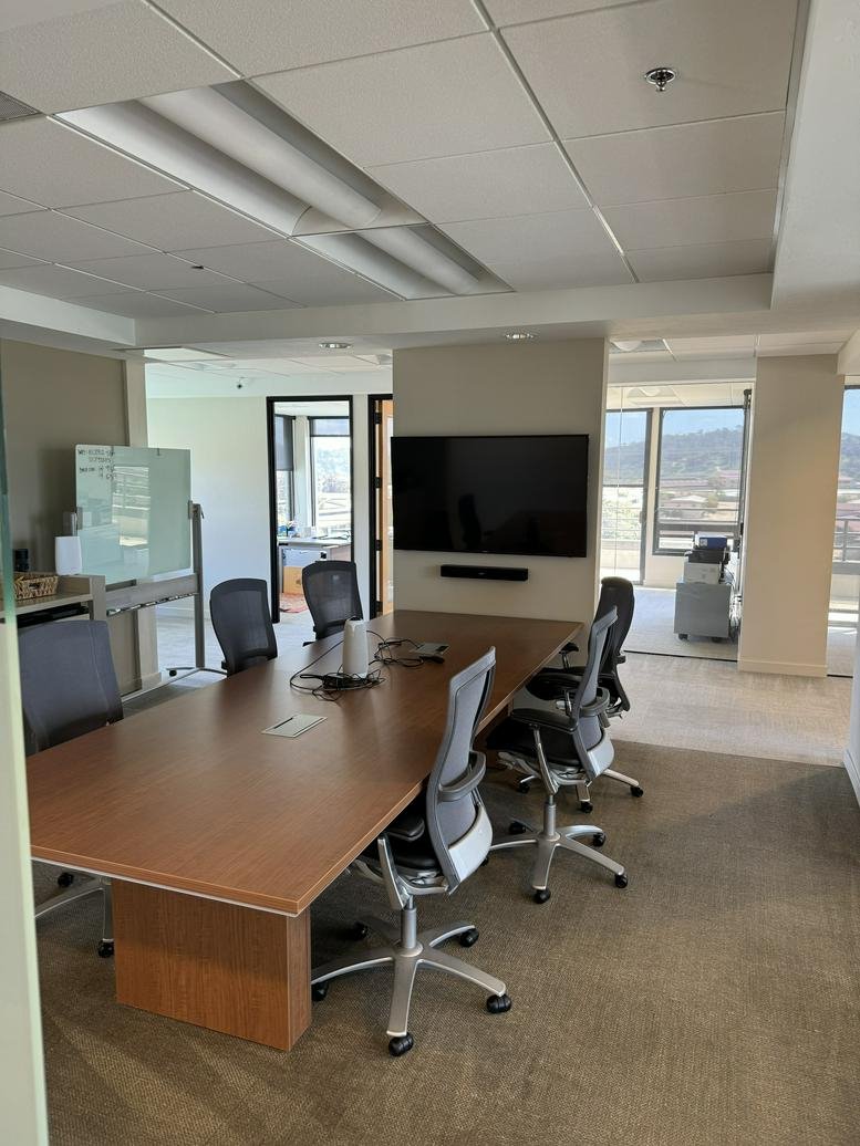 Professional meeting room with a large wooden table, ergonomic chairs, and wall-mounted monitor.