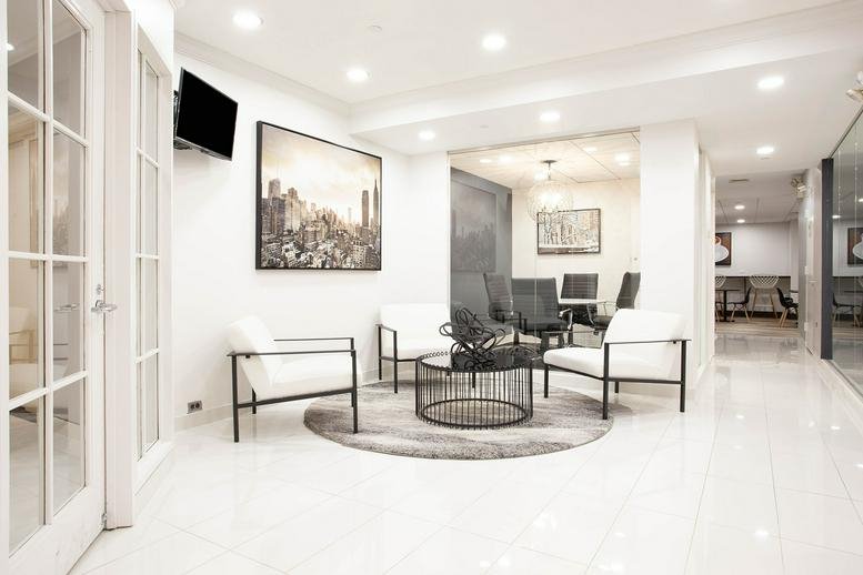 Bright reception and lounge area at 521 5th Avenue, New York City with white armchairs and city artwork.
