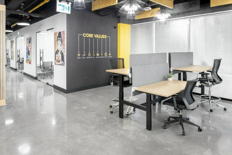 Modern communal workspace featuring height-adjustable desks and a black wall with core values text.