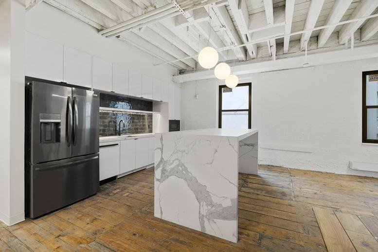 Modern communal kitchen at 53 Pearl Street featuring a marble island and dark stainless steel appliances.