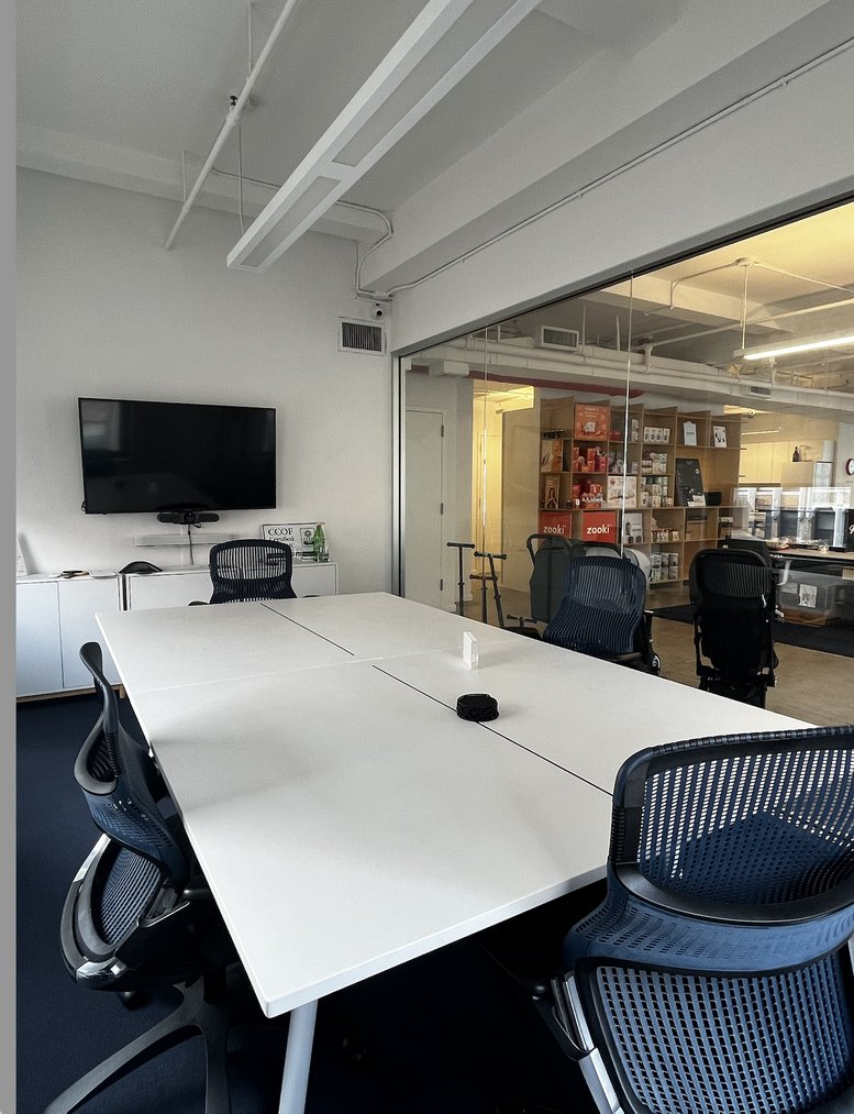 Meeting room at 535 8th Avenue with a large white table, blue mesh chairs, and a wall-mounted TV.