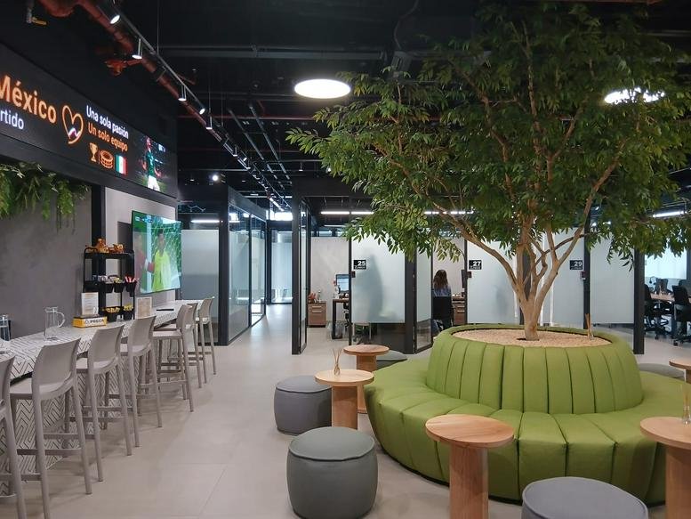 Spacious communal lounge at PREOS, 5420 Boulevard Reforma with a large indoor tree and green circular seating.