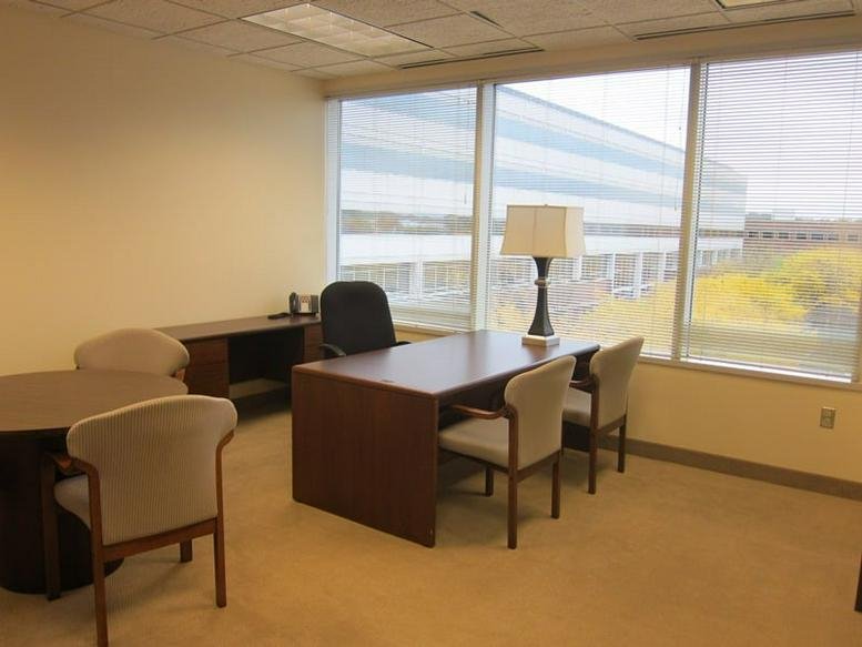 Private office featuring a wooden desk, a lamp, and large windows looking out at the 550 Cochituate Rd building.