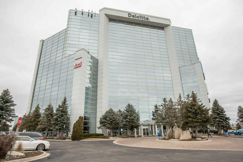 Modern office building facade with manicured landscaping and a paved entrance area.