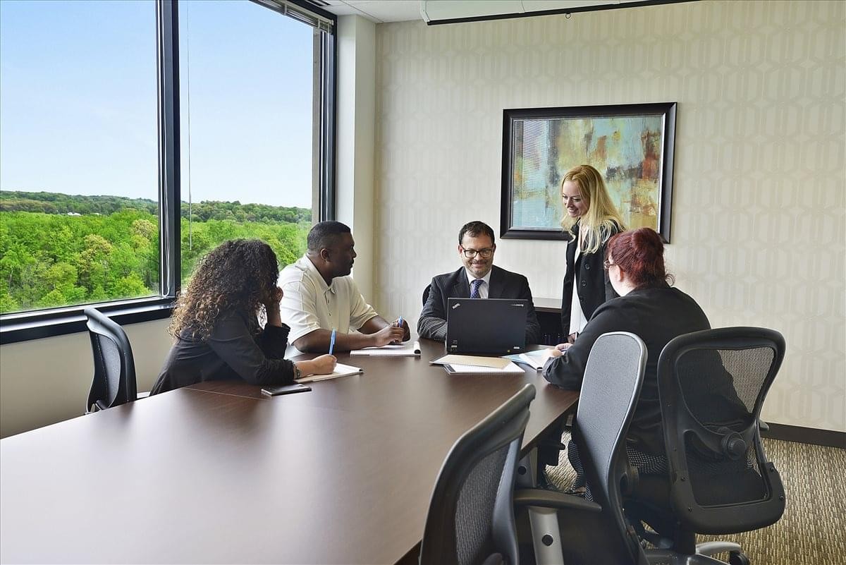 A professional meeting room at 5680 King Centre Dr. Suite 600 with large windows showing green views.