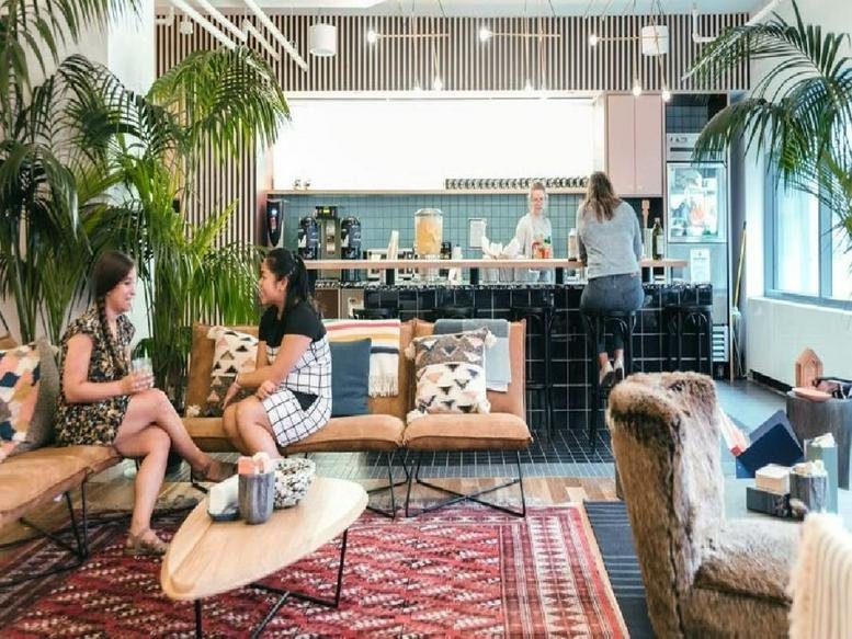 Spacious communal lounge featuring leather sofas, colorful rugs, and a coffee bar in the background.