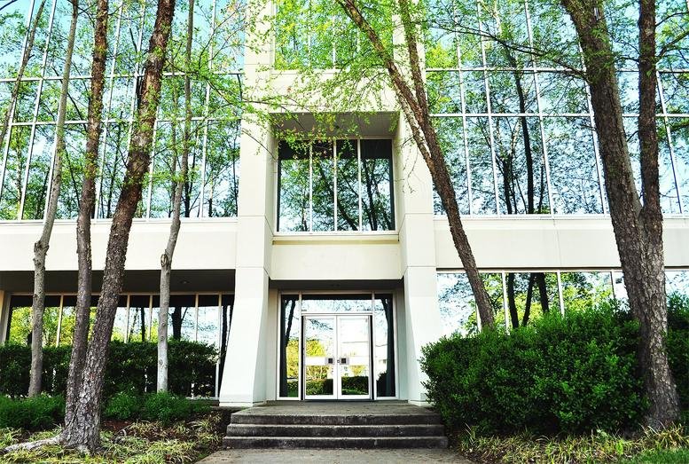 Exterior entrance of The Huntsville Hub building with tall trees and glass facade.