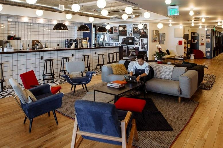 Bright office lounge with eclectic blue and red armchairs, a large grey sofa, and tile-fronted bar.