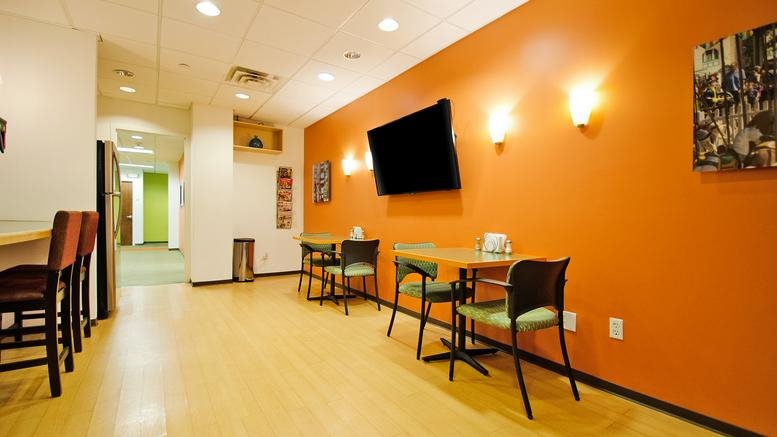 Spacious breakroom at 600 Mamaroneck Avenue with orange feature wall and dining tables.