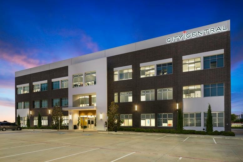 Evening exterior view of the modern brick and glass building with illuminated signage.