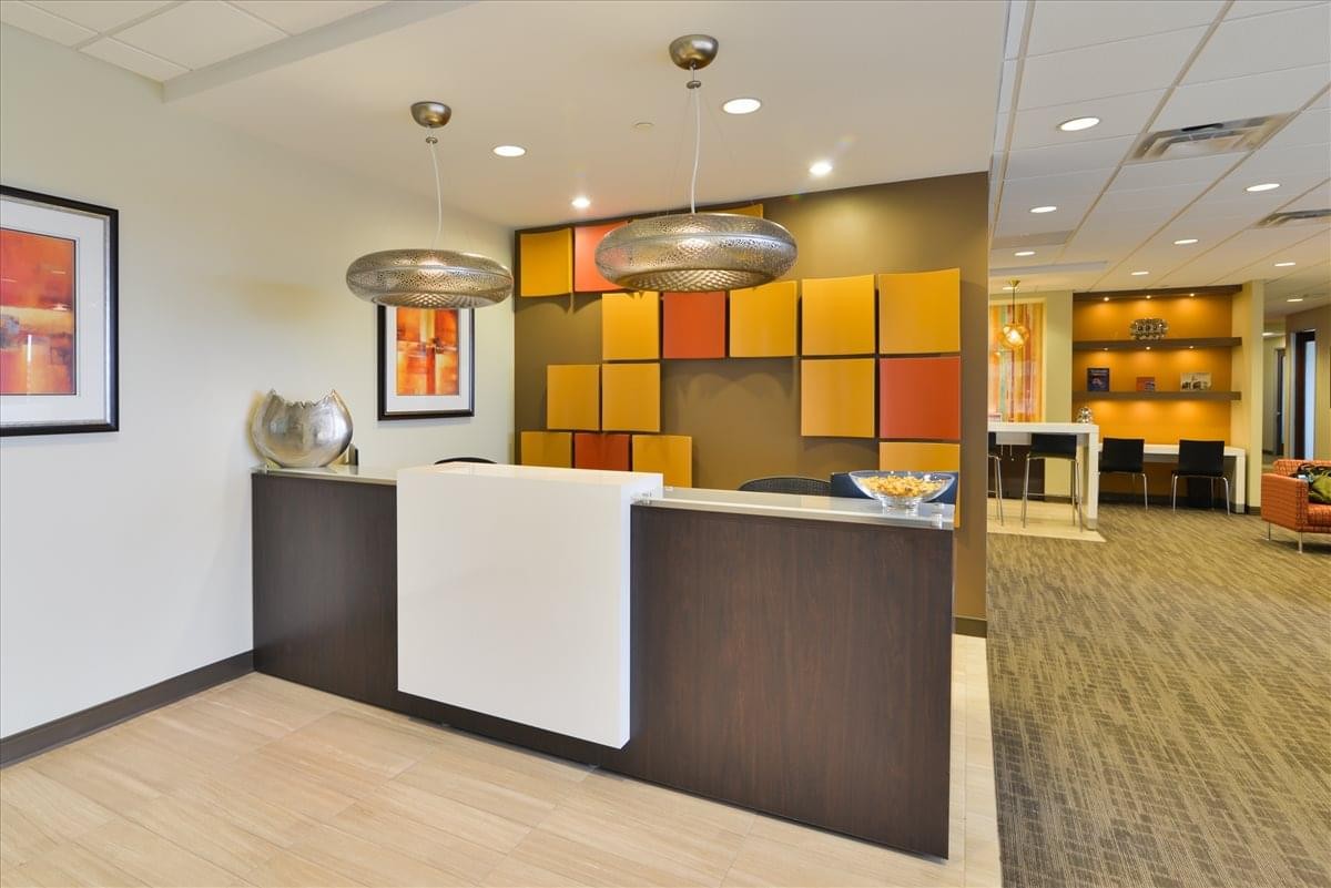 Reception area of Tuscany Plaza Business Center featuring a dark wood desk and colorful geometric wall art.