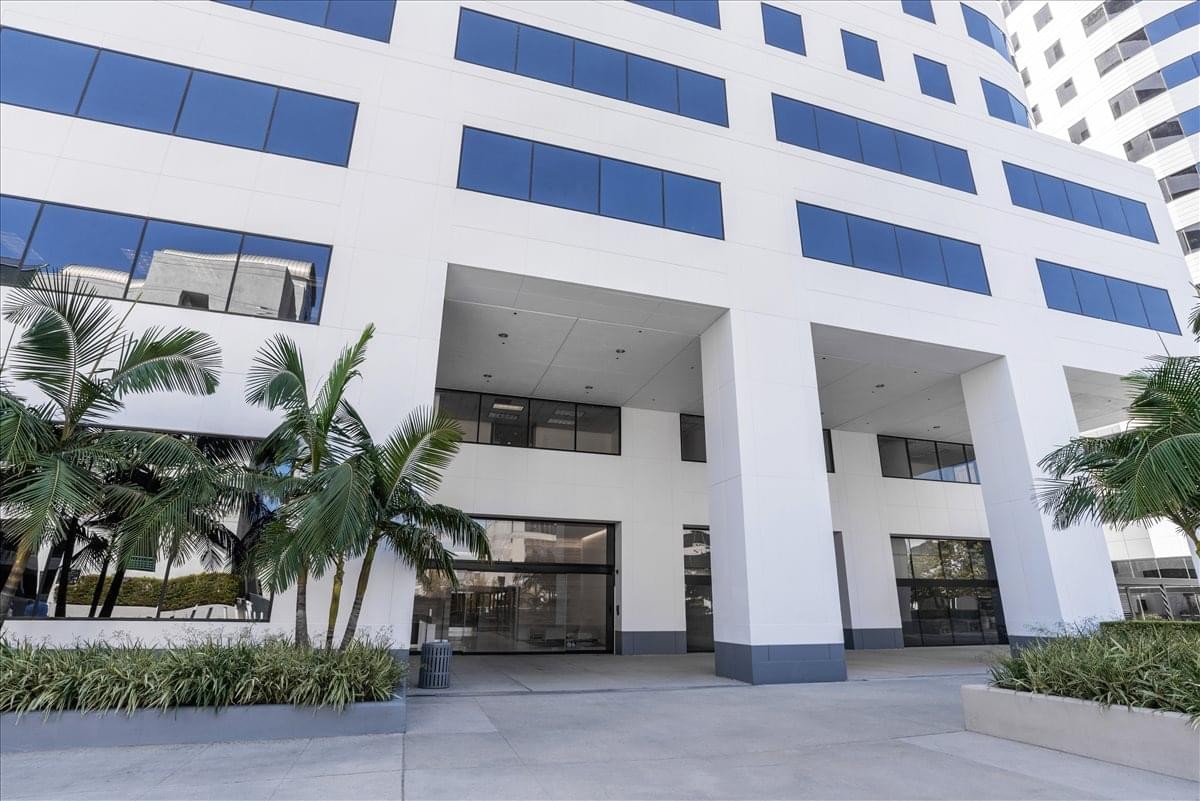 Exterior entrance and white facade of the Trillium Towers Center surrounded by palm trees.