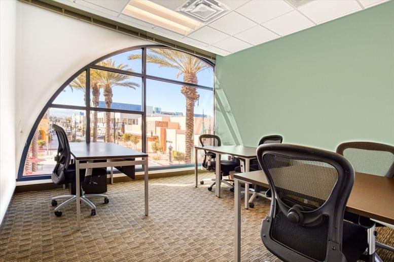 Workspace at 6671 S. Las Vegas Blvd. with desks, ergonomic chairs, and a large arched window with palm tree views.