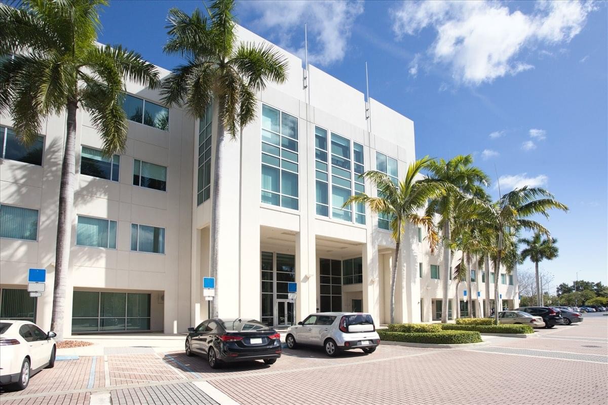 Exterior view of the modern white office building at 6750 N. Andrews Avenue with palm trees and blue sky.