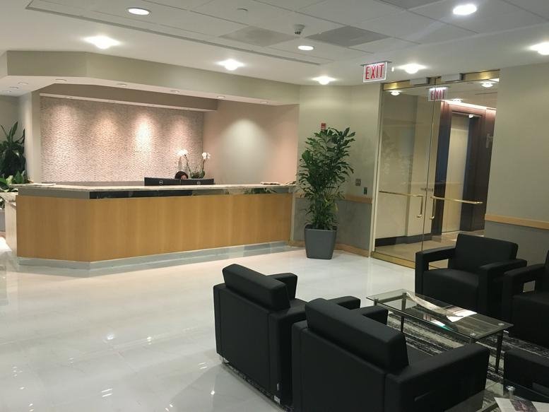 Bright reception area with a wooden front desk and black leather armchairs.