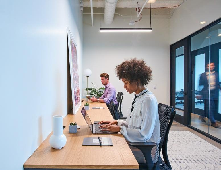 Common area at 717 Texas Avenue featuring a long desk, laptop-using professional, and glass doors.