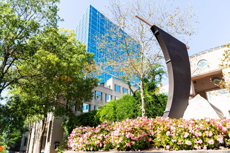 Exterior view of the blue glass building at 7200 Wisconsin Avenue behind lush trees and pink flowers.