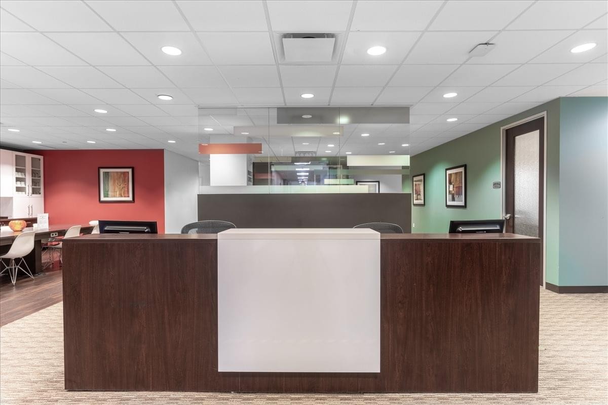 Professional reception desk with a dark wood finish and white center panel in a brightly lit lobby.