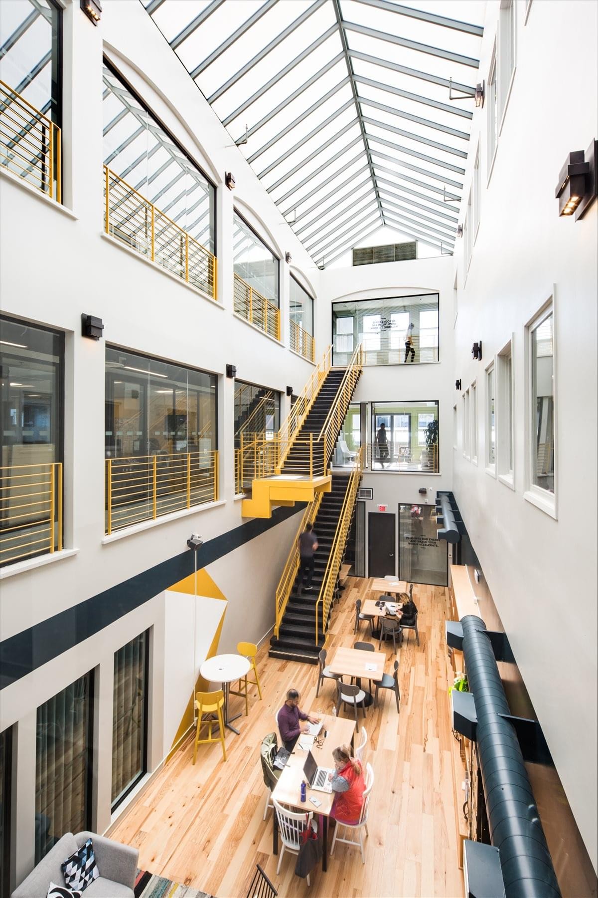 Wide-angle view of a multi-level atrium workspace at Spaces Santa Monica with a skylight and yellow stairs.