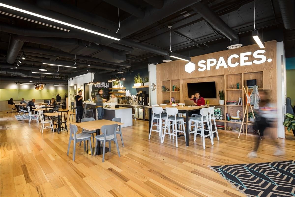 Wide-angle view of the vibrant communal lounge at Spaces Santa Monica with the branded logo wall.
