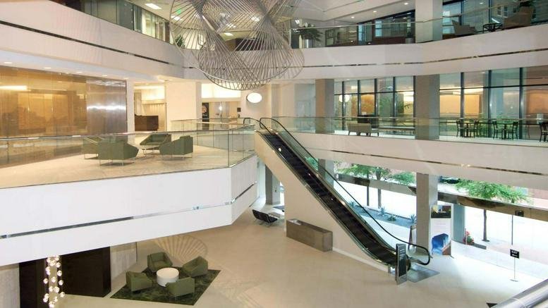 Spacious multi-level building lobby with an escalator, glass railings, and seating areas.