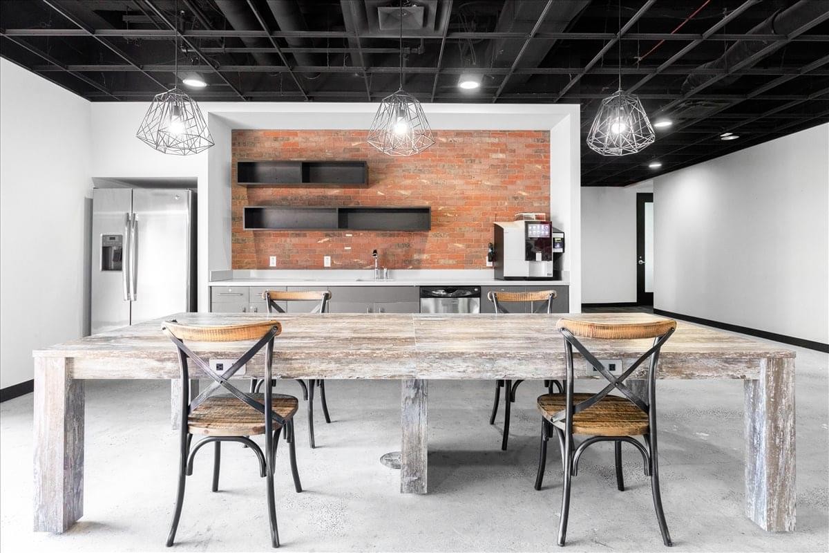 Modern communal kitchen at Sevens Building with brick feature wall and rustic wooden table.