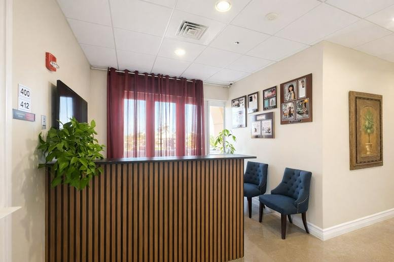 Bright reception area with a slatted wood desk, blue velvet chairs, and a large plant.